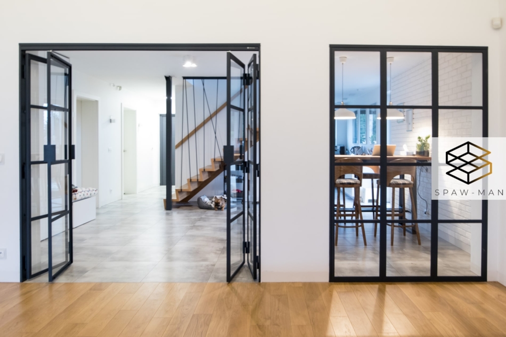 Stalowa ściana szklana z drzwiami harmonijkowymi między kuchnią a salonem w kolorze czarnym.
