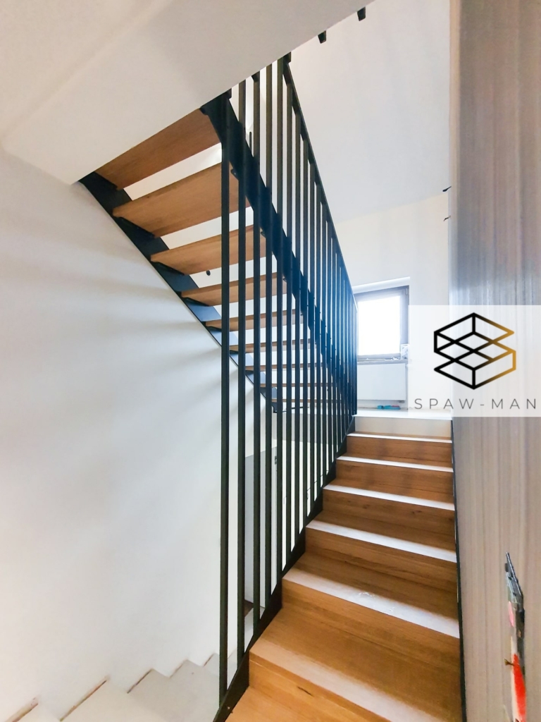 Stalowe schody z podestem, pełnymi policzkami, stopniami z drewna dębowego oraz balustradą o liniowym ułożeniu.