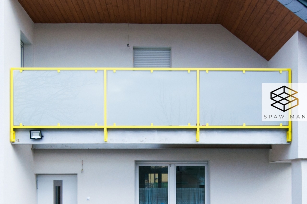 Balustrada balkonowa w żółtym kolorze z wypełnieniem ze szkła mlecznego mocowana od czoła balkonu.